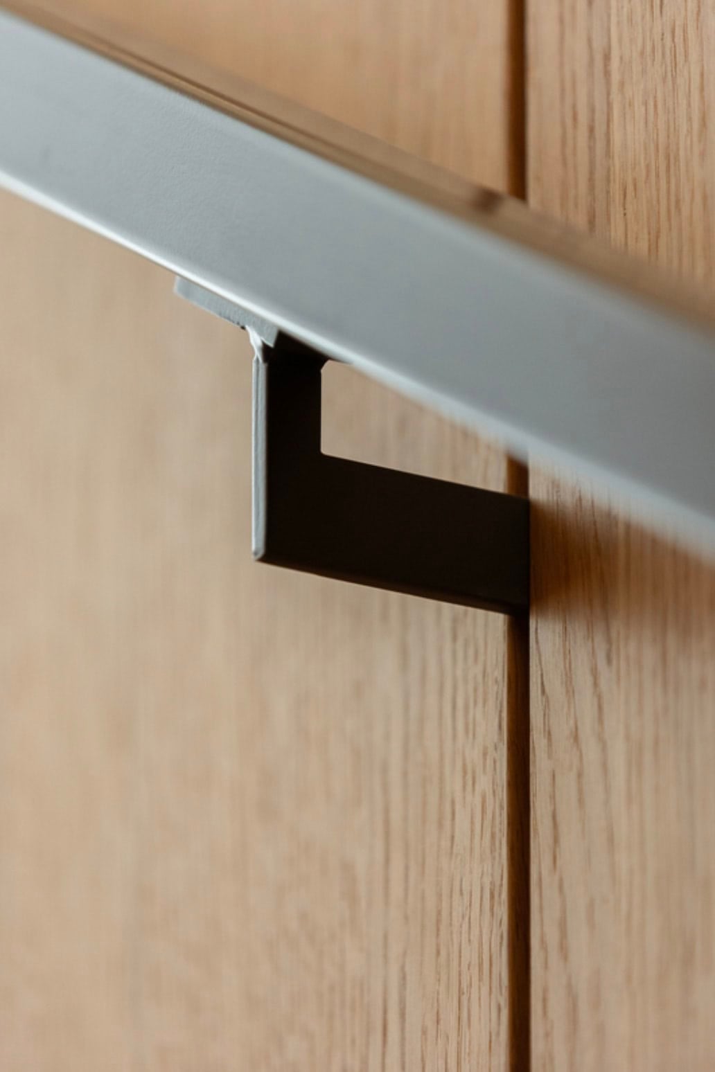 Close-up of a powder-coated steel handrail bracket mounted on vertical wood paneling