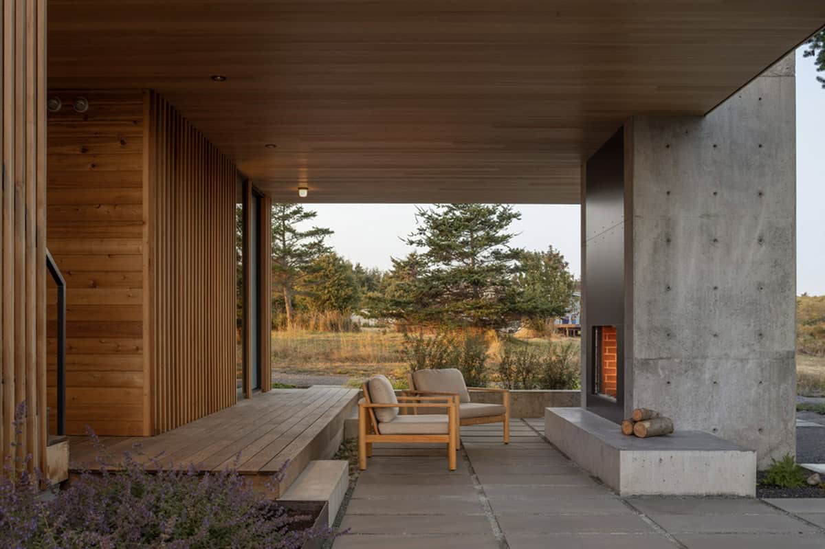 Covered patio with an outdoor fireplace, lounge chairs, and a view of cedar siding and surrounding trees