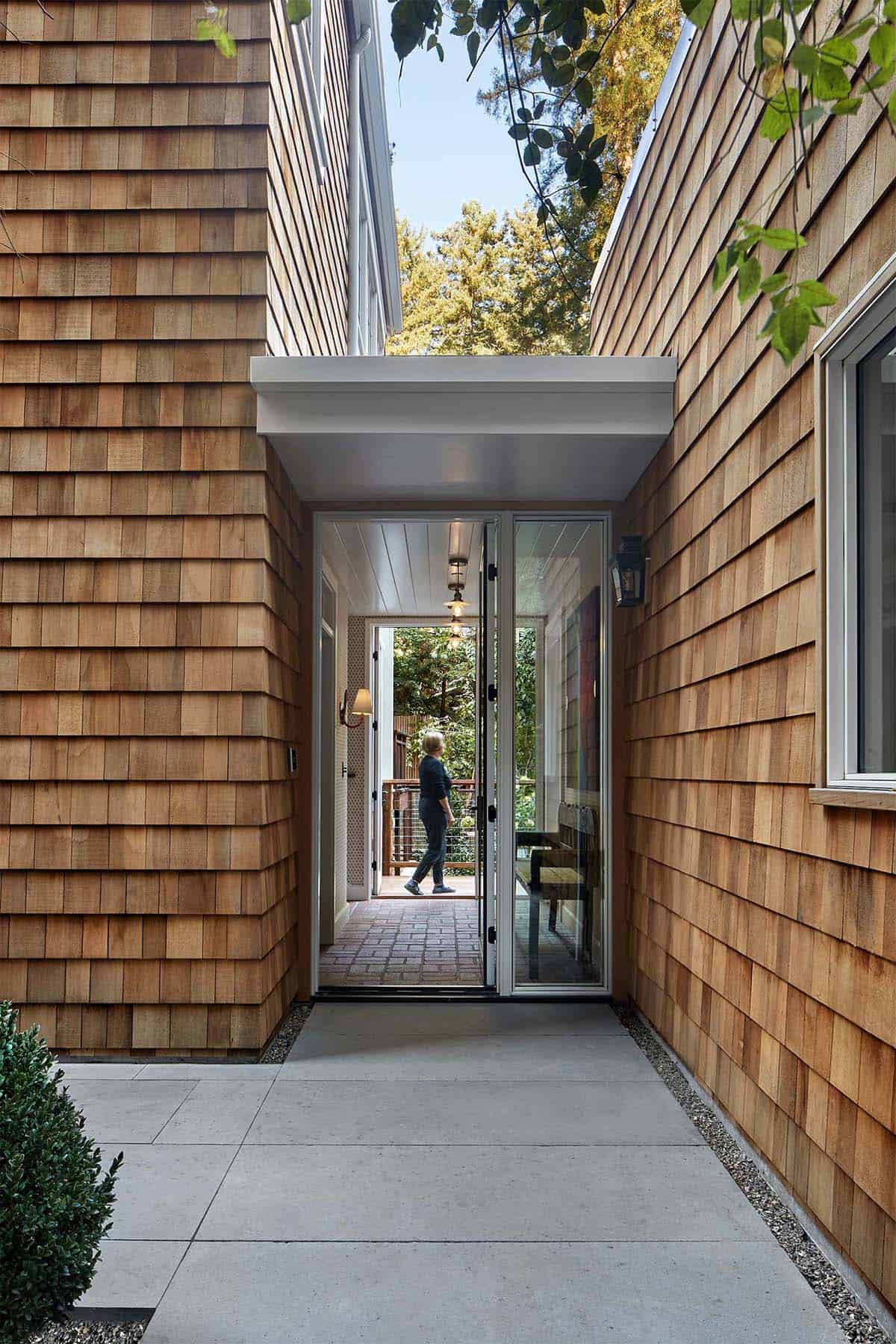 Modern glass entry door set between cedar shingle walls with a covered walkway