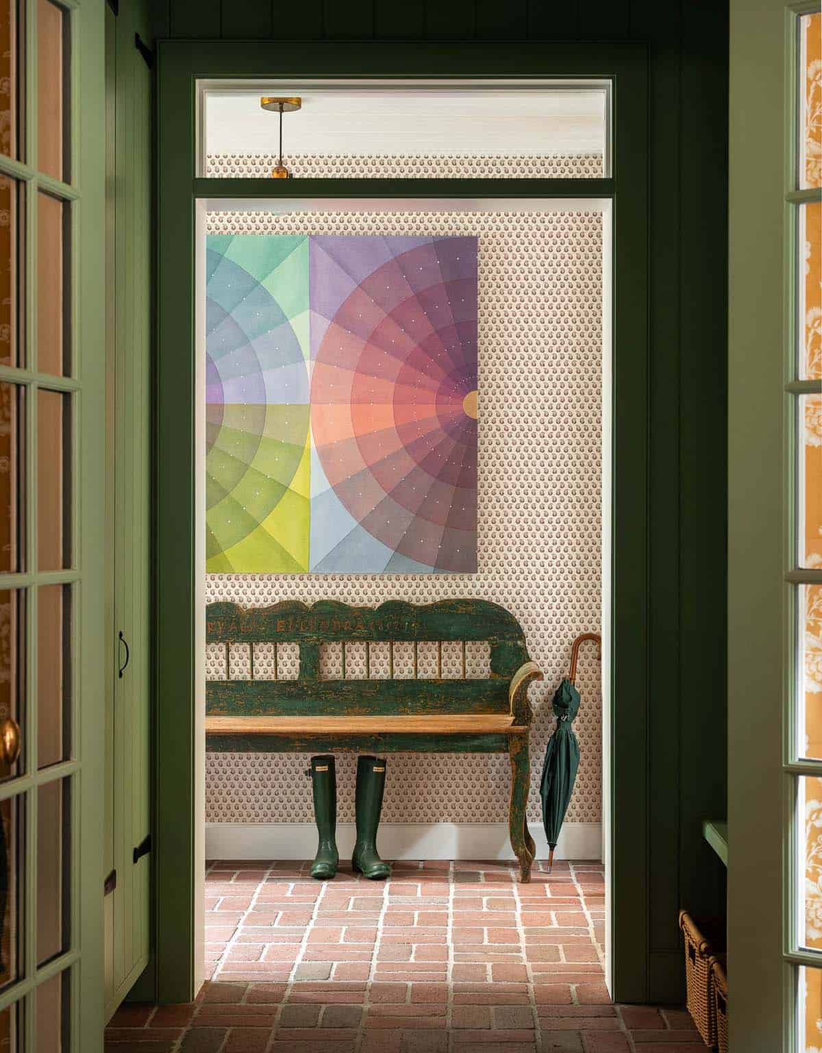 Mudroom entry with brick floor, green painted door, colorful abstract artwork, and a distressed wooden bench