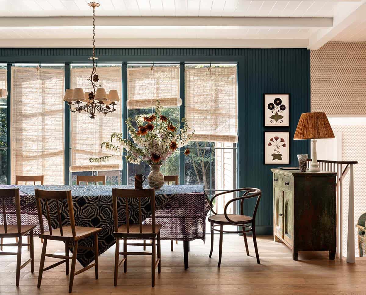 Dining room with teal painted wall, bamboo shades, mixed wood chairs, and a bold patterned tablecloth