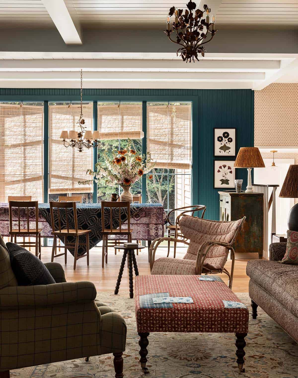 Open plan living and dining area with teal accent wall, eclectic patterned furnishings, and a floral chandelier
