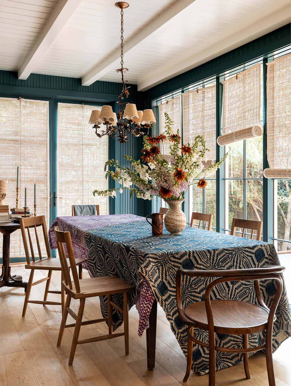 Dining table with bold indigo patterned cloth, mixed wood chairs, and wildflower arrangement beneath a decorative chandelier