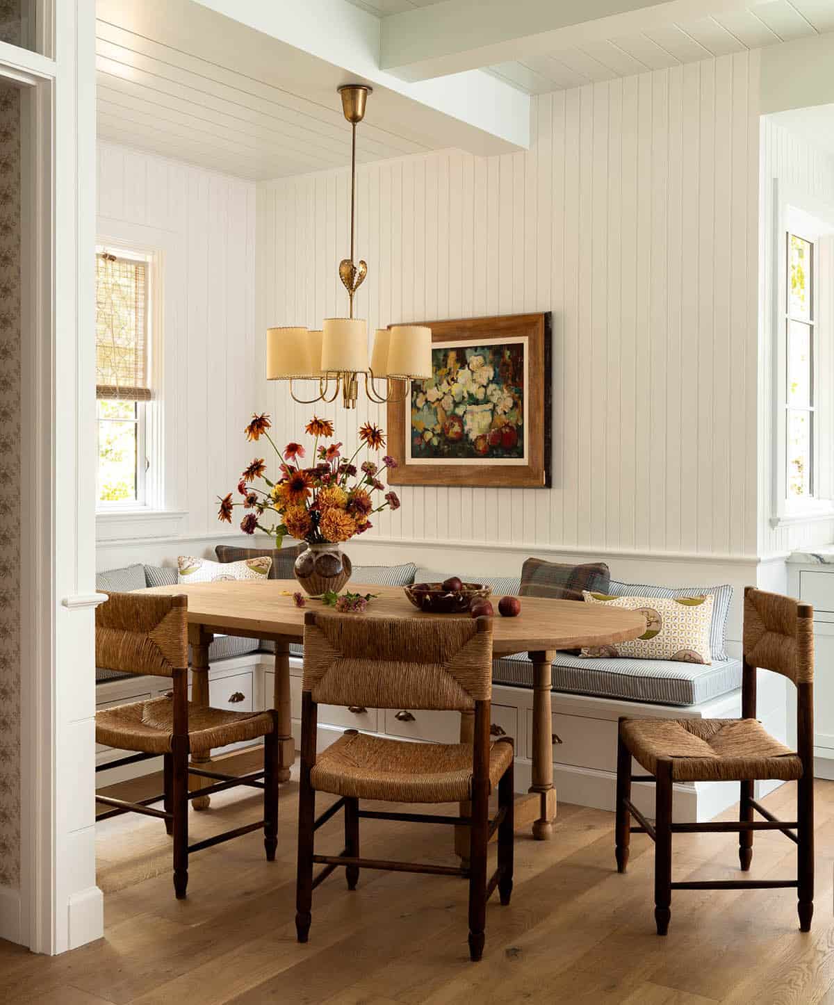 Breakfast nook with built-in bench seating, rush seat chairs, oval wood table, and brass chandelier