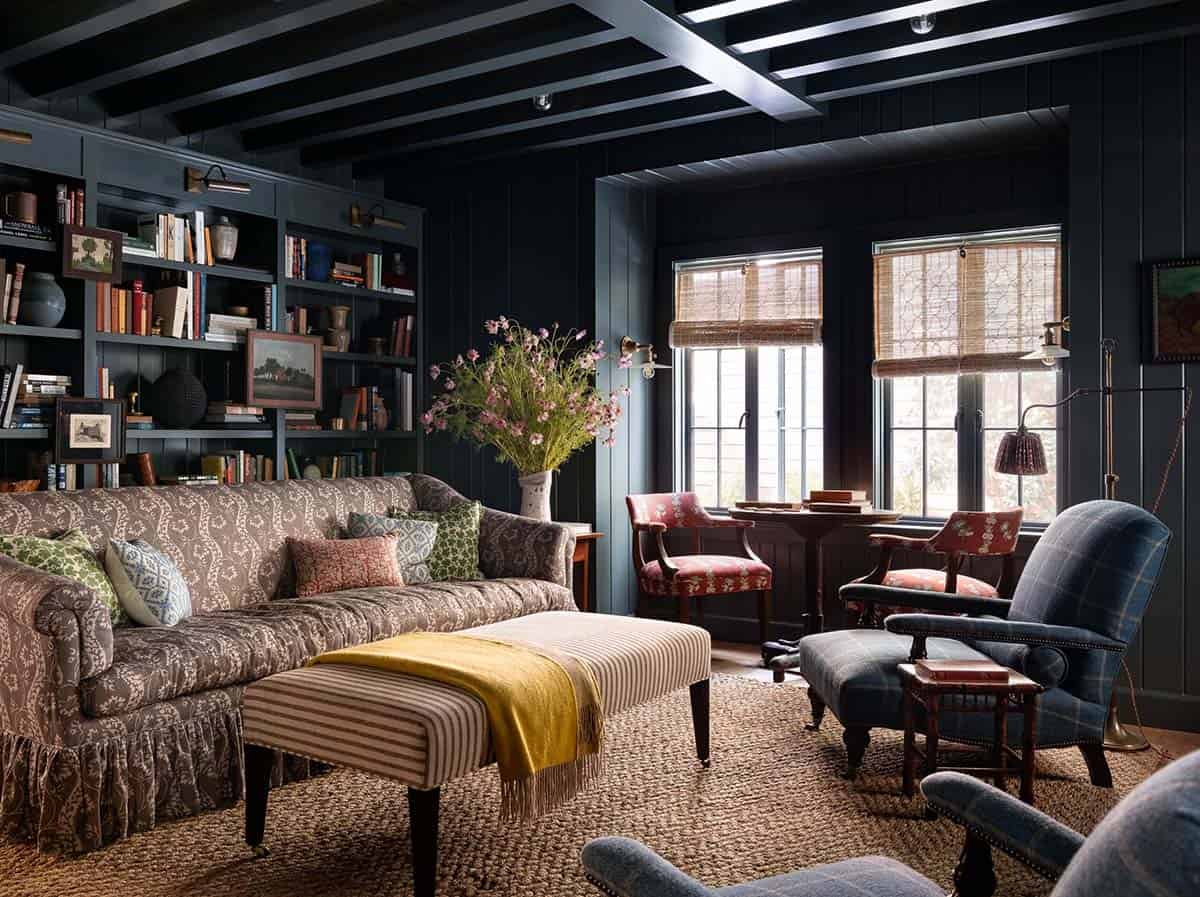 Moody dark navy library with floor-to-ceiling bookshelves, patterned sofa, and layered vintage seating