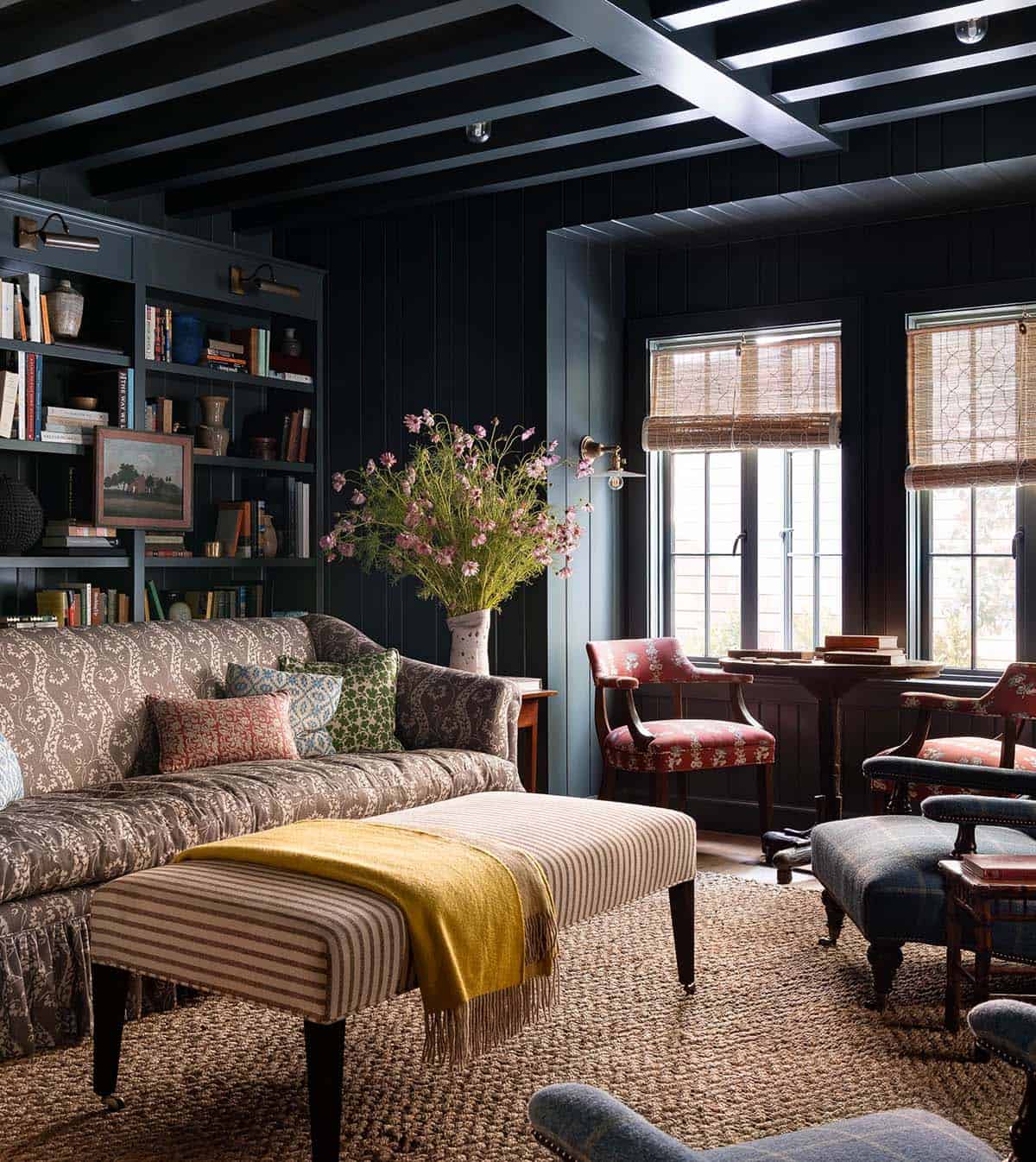 Dark paneled study with built-in bookshelves, patterned sofa, striped ottoman, and yellow throw