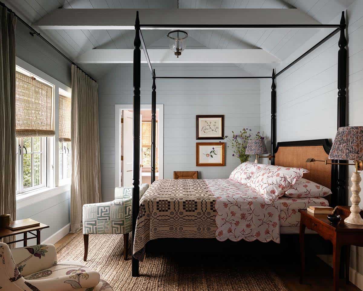 Primary bedroom with black four-poster bed, cathedral ceiling, woven rug, and botanical prints on pale blue walls