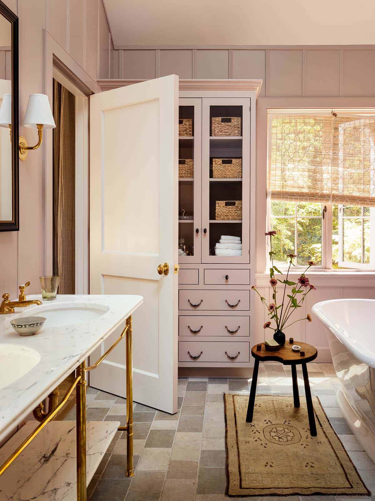 Pink bathroom with freestanding soaking tub, brass fittings, tall linen cabinet, and slate tile floor