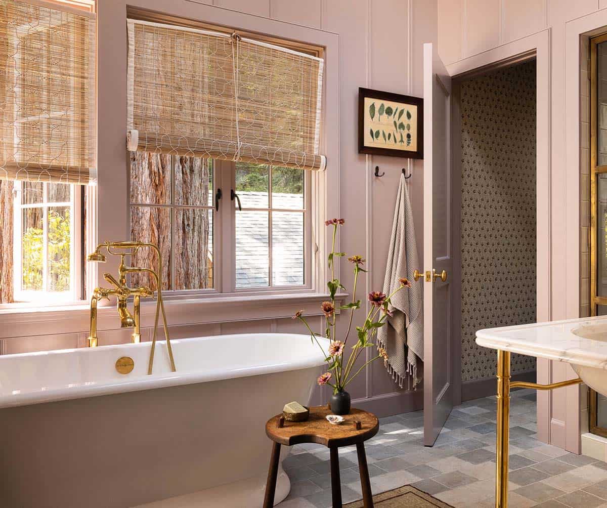Pink primary bathroom with clawfoot tub, brass floor-mounted faucet, bamboo shades, and redwood tree views