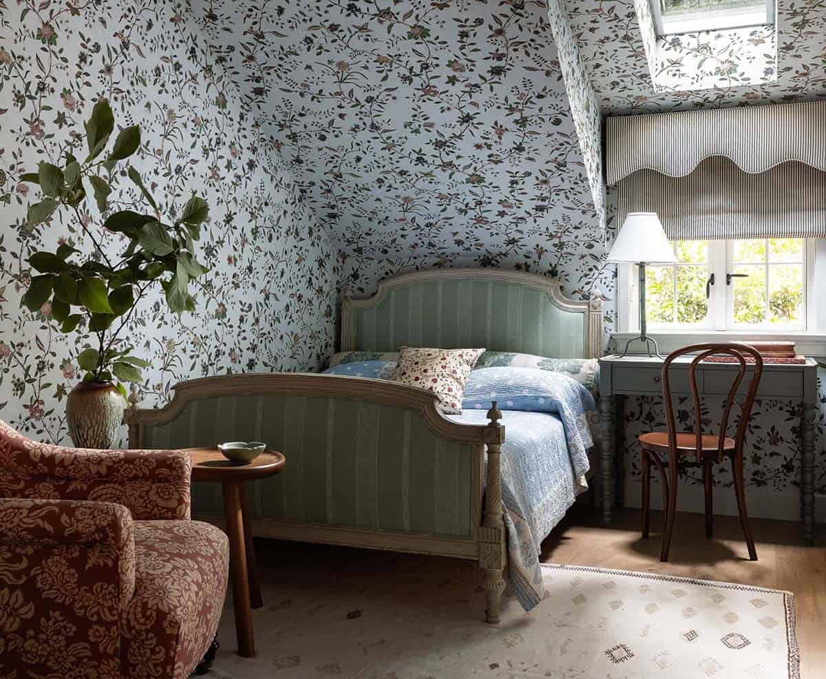 Guest bedroom with all-over floral wallpaper continuing onto the ceiling, sage green bed frame, and striped roman shade