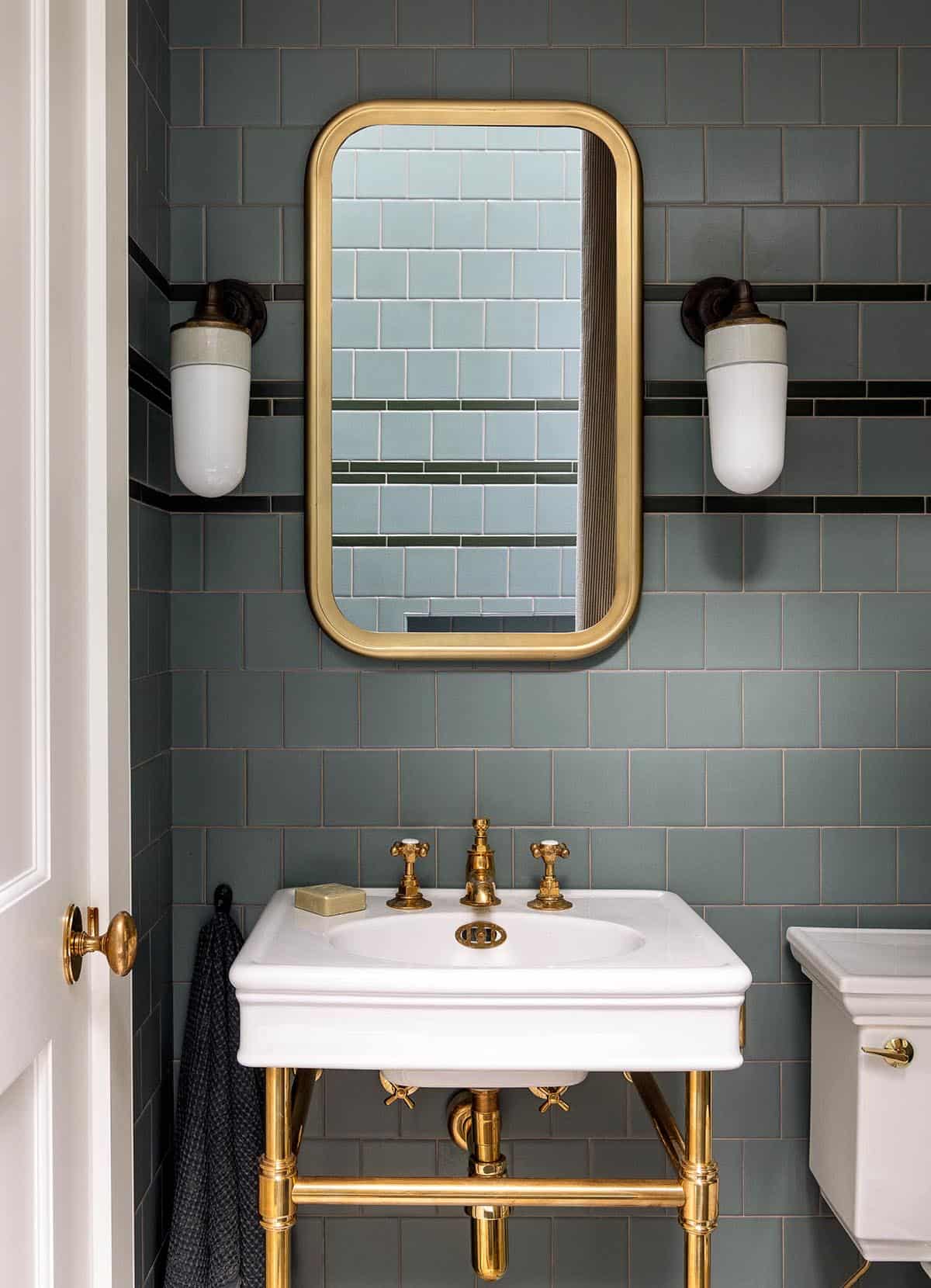 Bathroom vanity with sage green subway tile, brass-framed mirror, and porcelain sink on brass legs