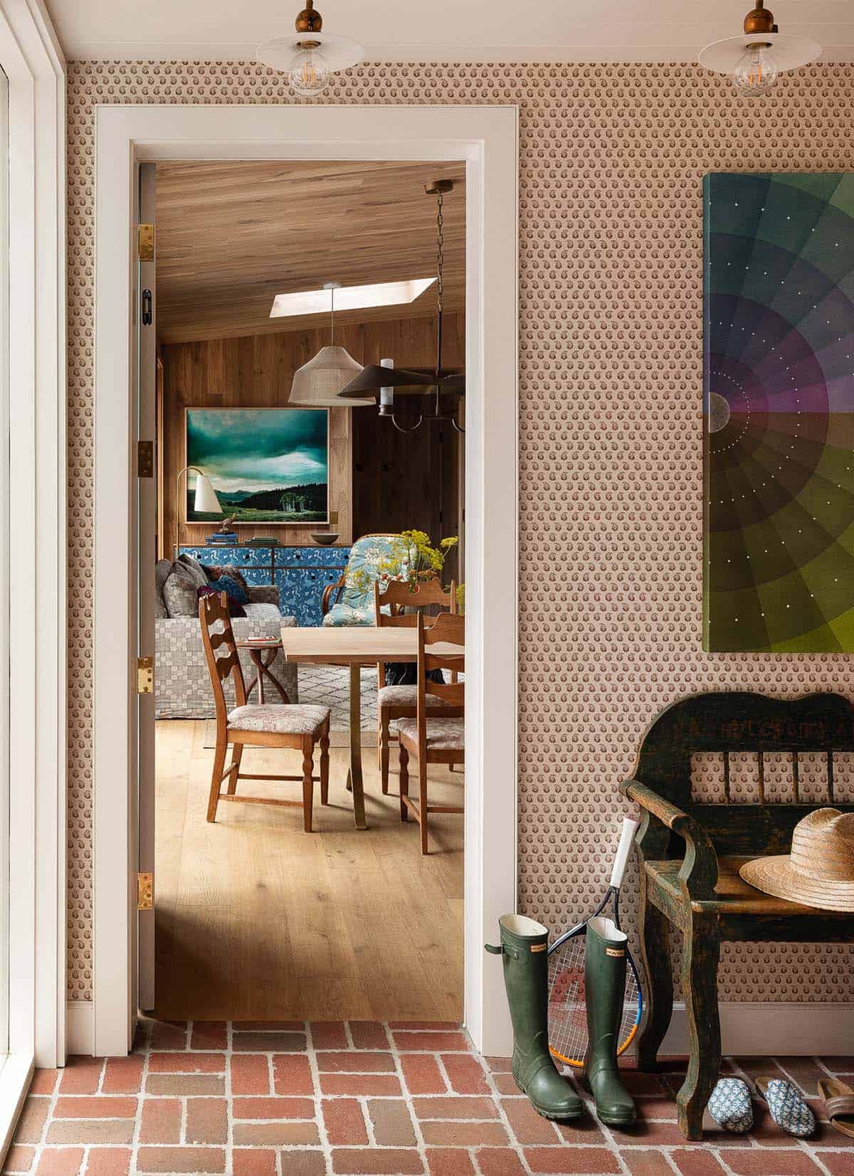 Entry mudroom with small-print wallpaper, brick floor, antique bench, and view into wood-paneled dining room