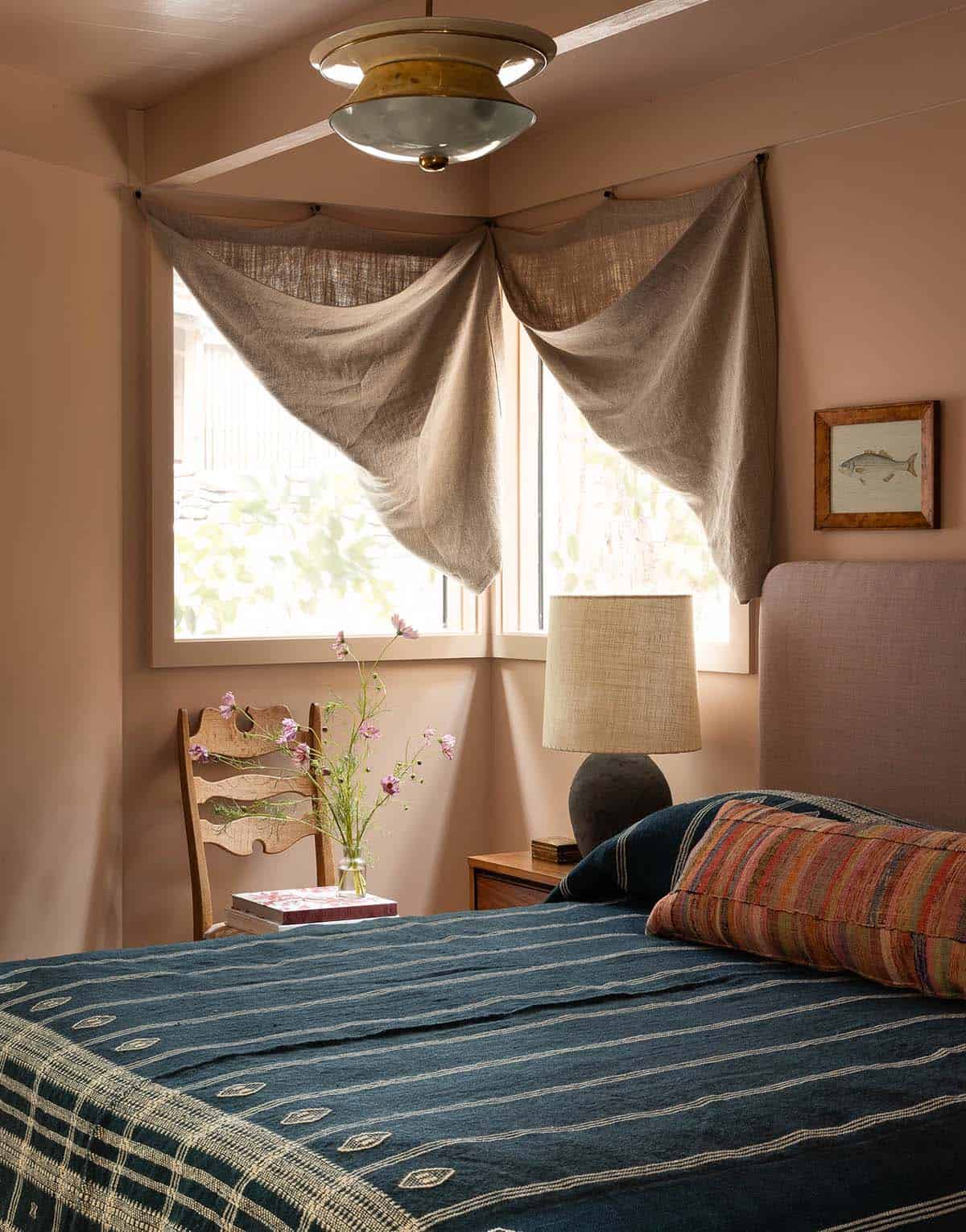 Terracotta-walled bedroom with draped linen curtains, blue woven bedspread, and vintage fish print