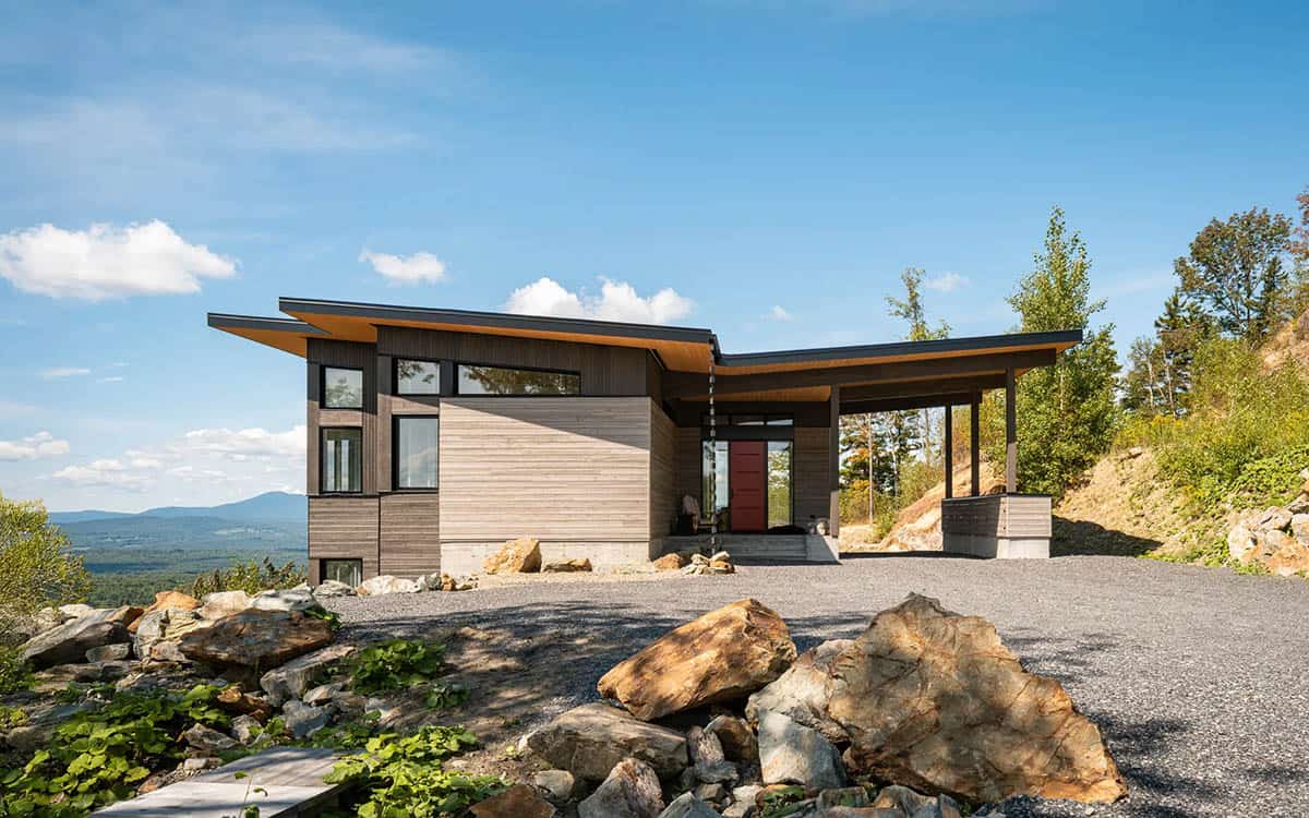 Modern cliffside house with cedar siding and red front door, set against mountain valley views