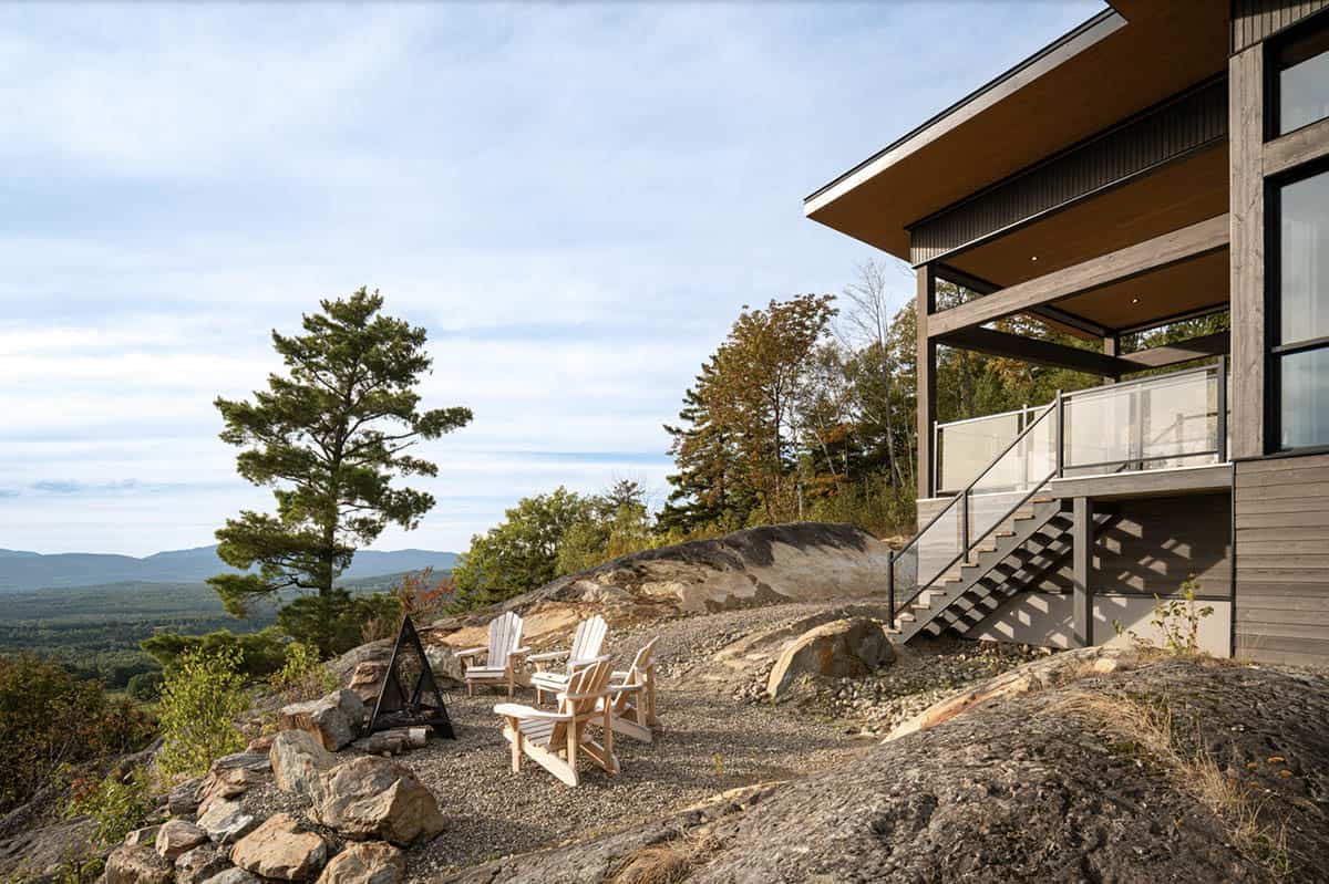 Adirondack chairs and fire pit on rocky outcrop beside house with glass balcony and staircase