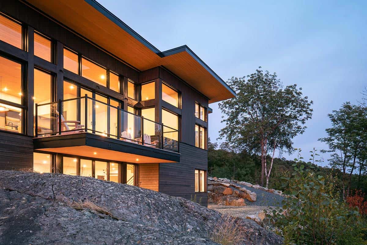 Close-up dusk view of glowing two-story house with floor-to-ceiling windows and glass balcony railing