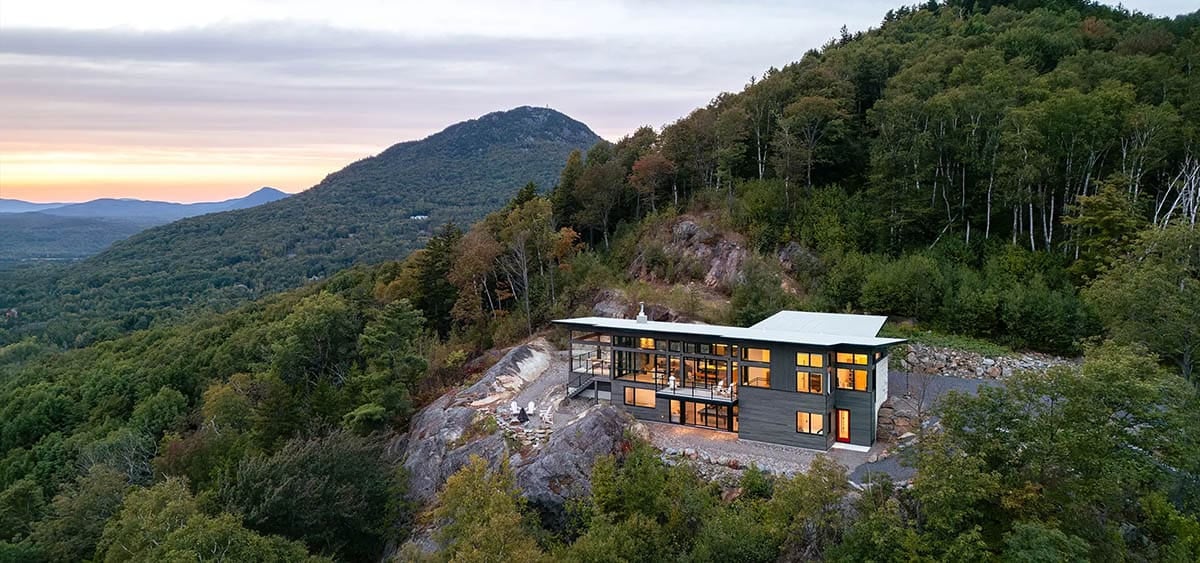 Wide aerial sunset view of modern cliffside home overlooking forested mountain valley