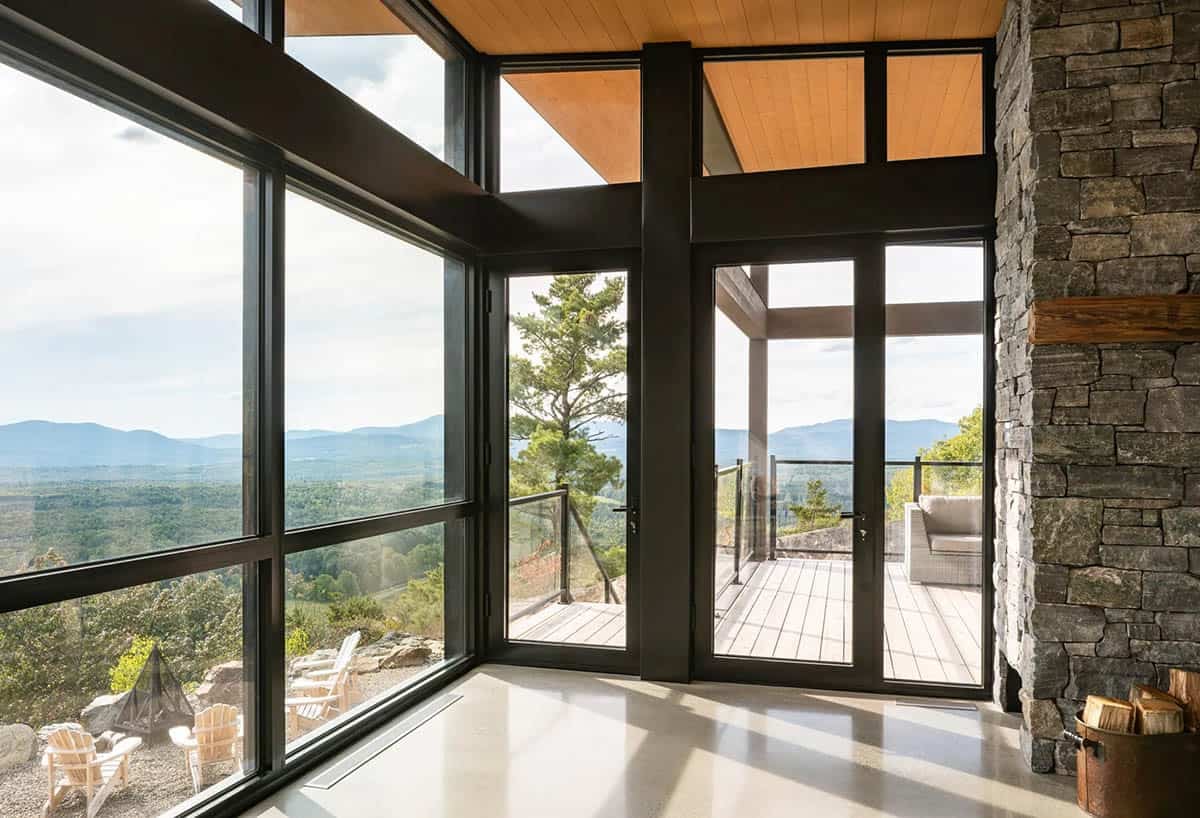 Interior corner window wall with black frames overlooking mountain valley and outdoor deck
