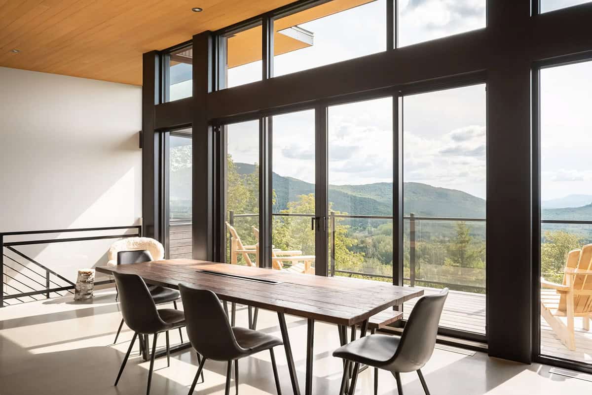 Dining area with rustic wood table and floor-to-ceiling windows framing mountain panorama