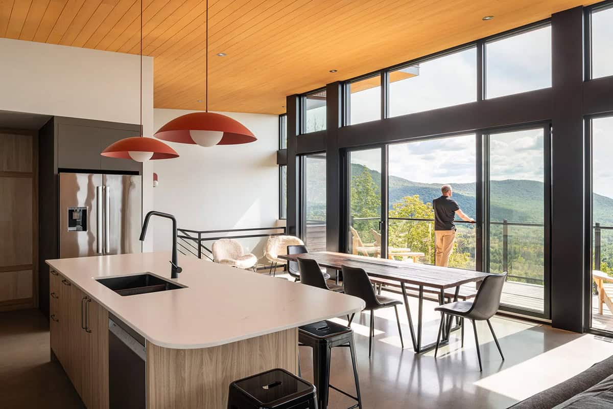 Open-plan kitchen and dining area with red pendant lights and person standing at glass balcony door