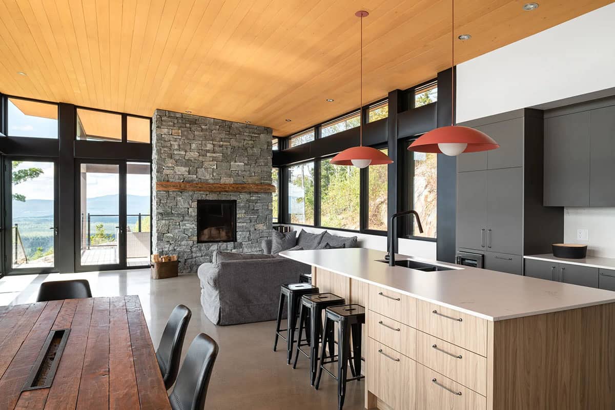 Open living space with stone fireplace, wood ceiling, red pendant lights, and wraparound windows
