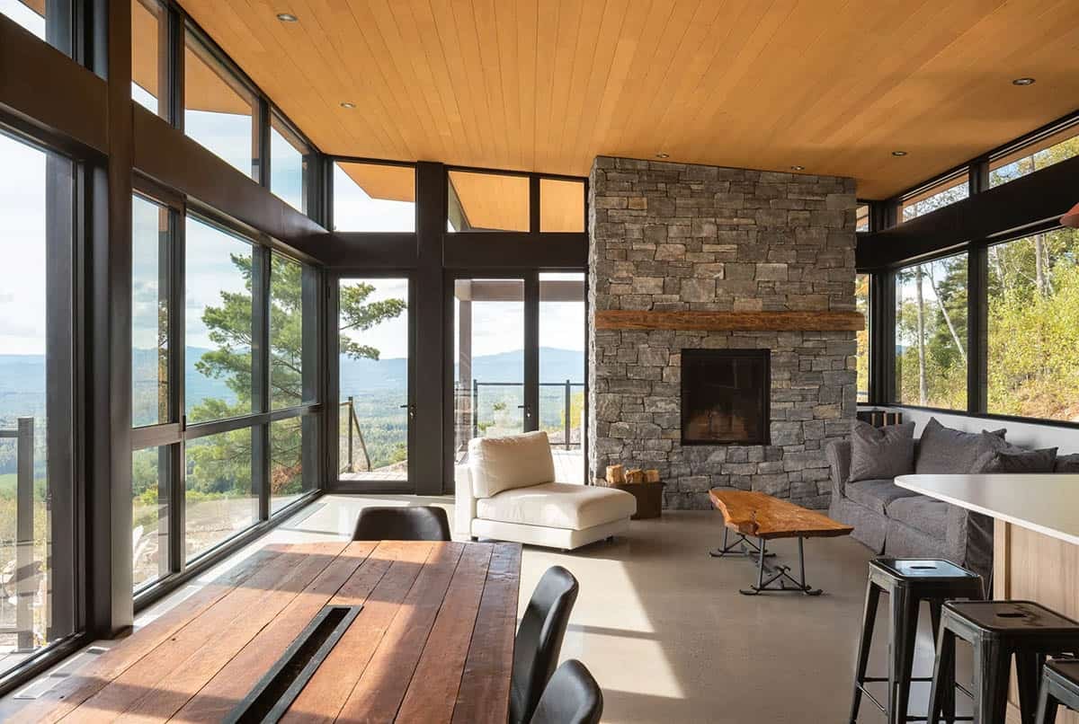 Living room with stone fireplace, live-edge coffee table, and glass walls facing forested hillside