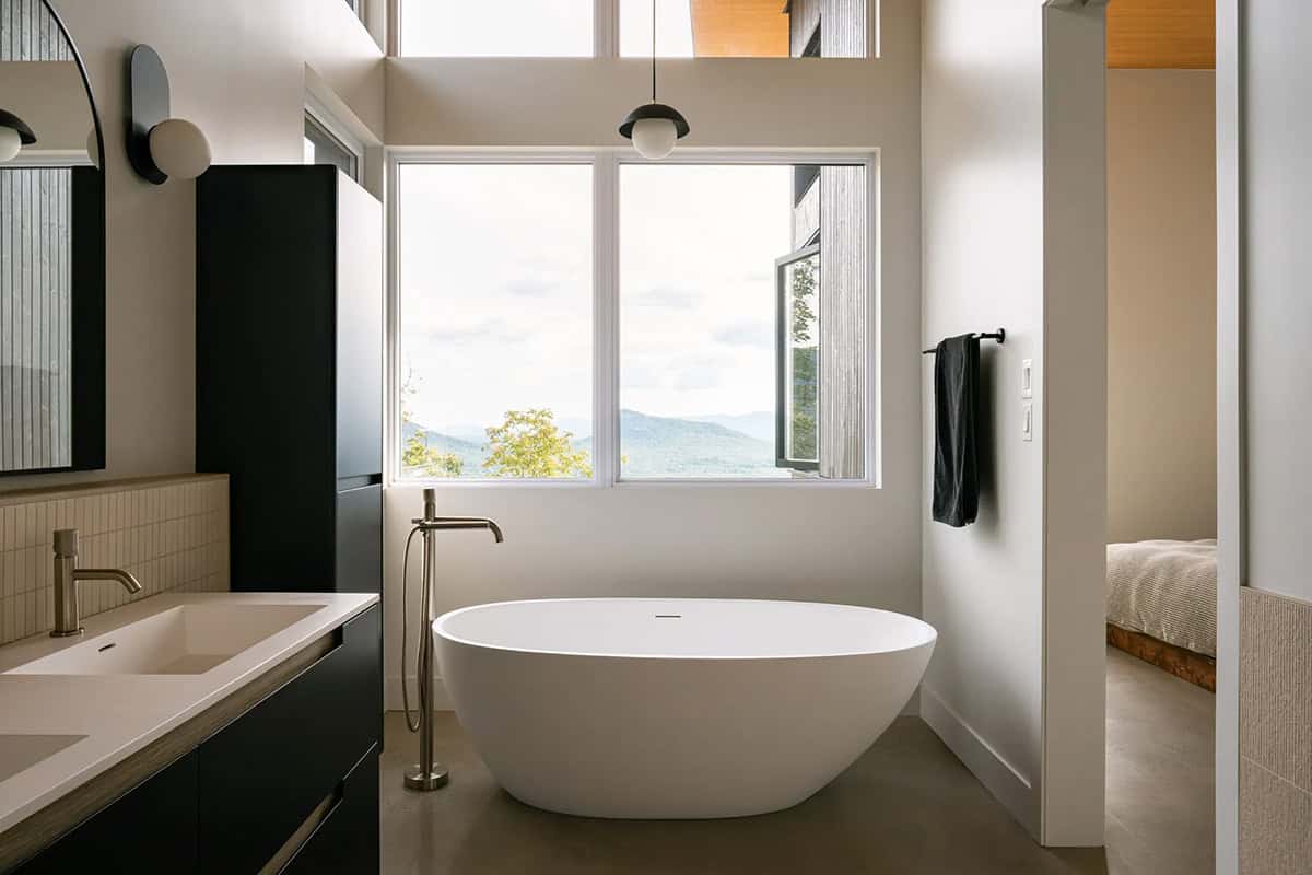 Modern bathroom with freestanding white soaking tub positioned beneath mountain-view window