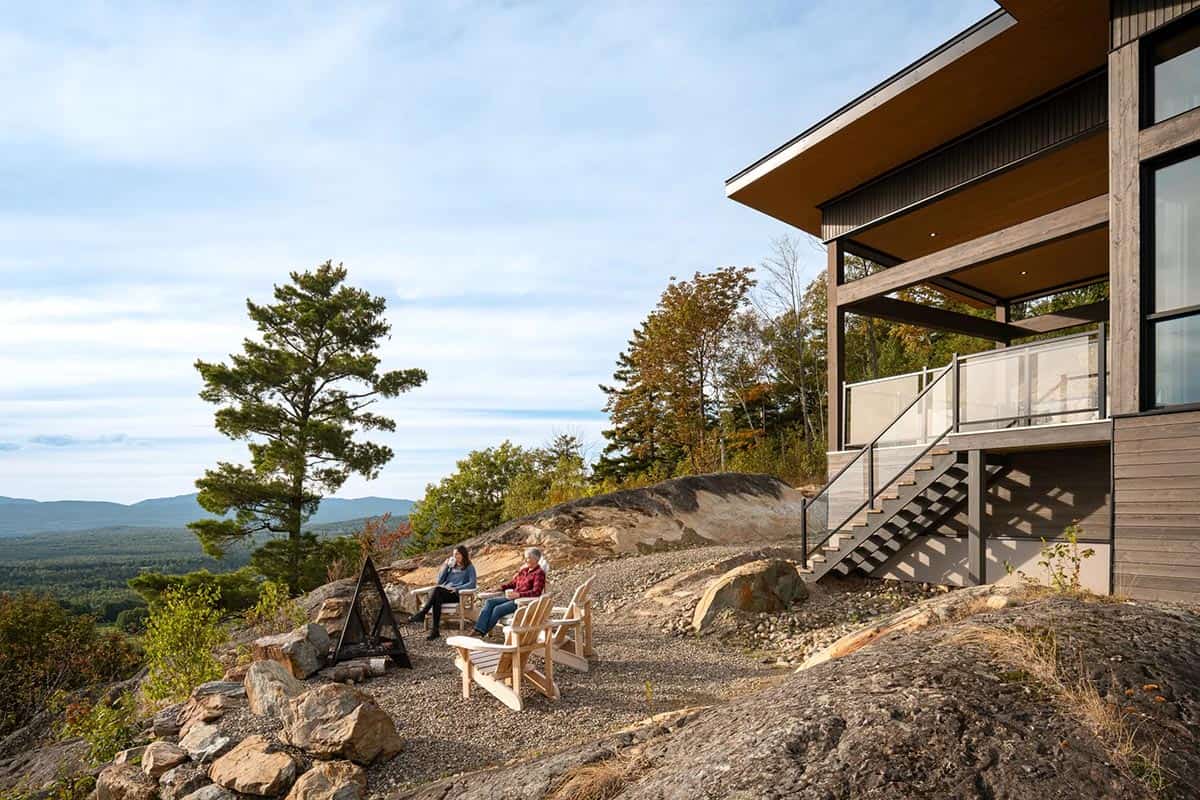 Couple seated in Adirondack chairs by fire pit beside house with mountain valley views