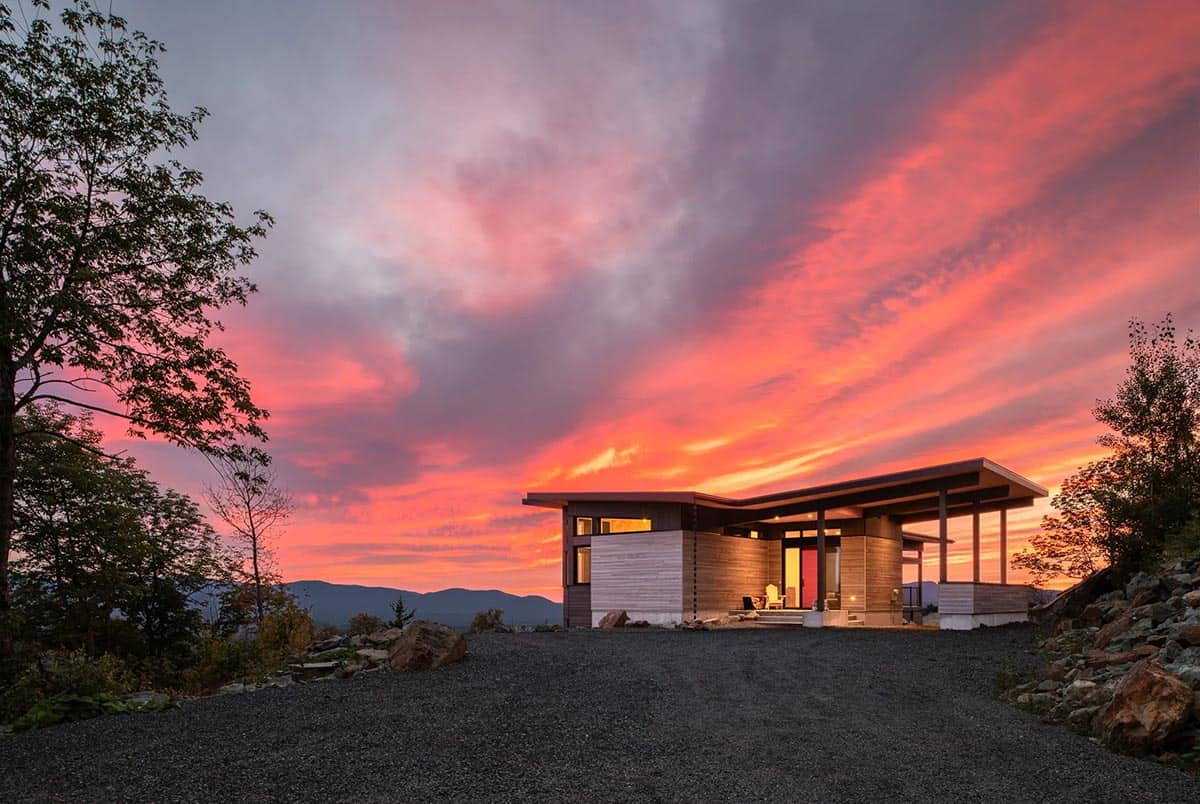 Wide-angle front view of single-story entry pavilion silhouetted against fiery sunset