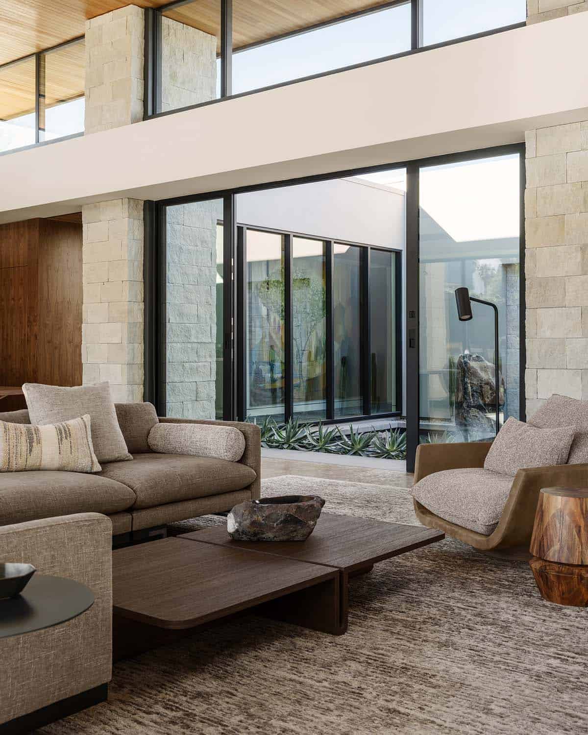 Living room with stone accent walls, gray sectional sofa, and sliding glass doors leading to a courtyard garden with agave plants