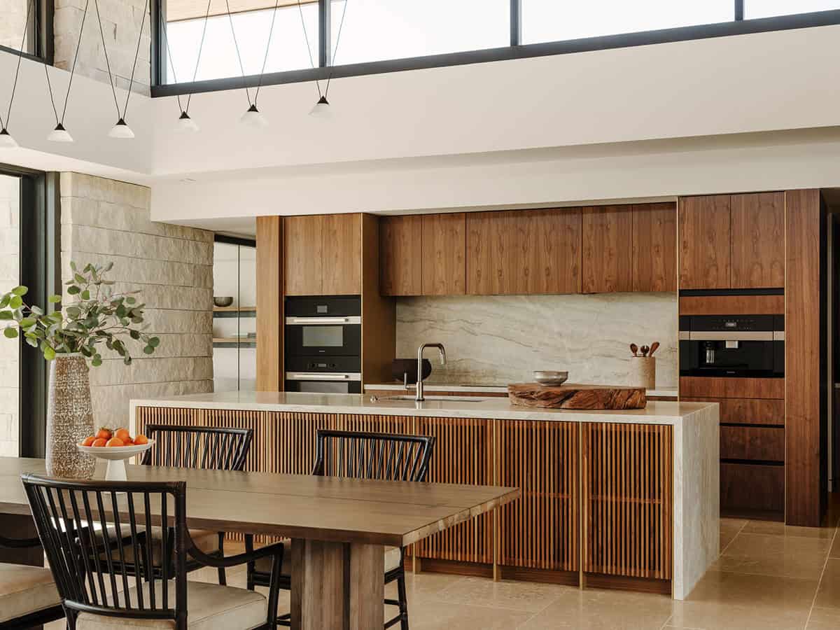 Modern kitchen with walnut cabinetry, slatted wood island, stone backsplash, and clerestory windows with pendant lighting