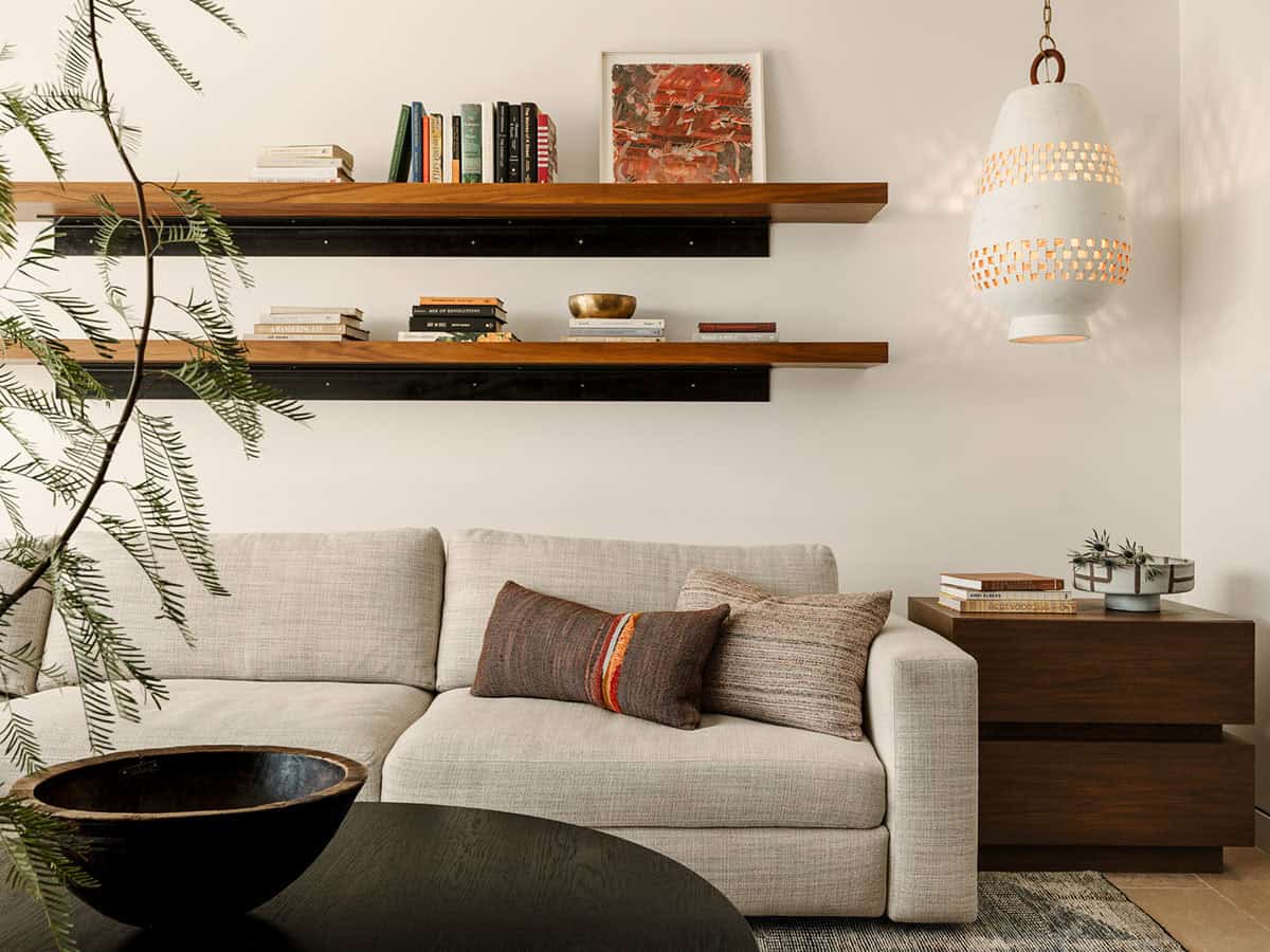 Casual living room with cream linen sofa, walnut floating shelves styled with books and art, and woven ceramic pendant light