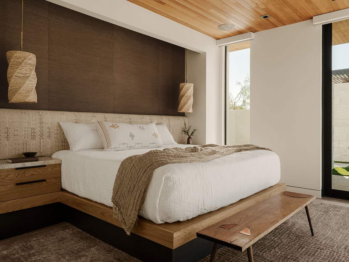 Primary bedroom with wood-plank ceiling, upholstered headboard, woven rattan pendants, and sliding glass door to a private courtyard