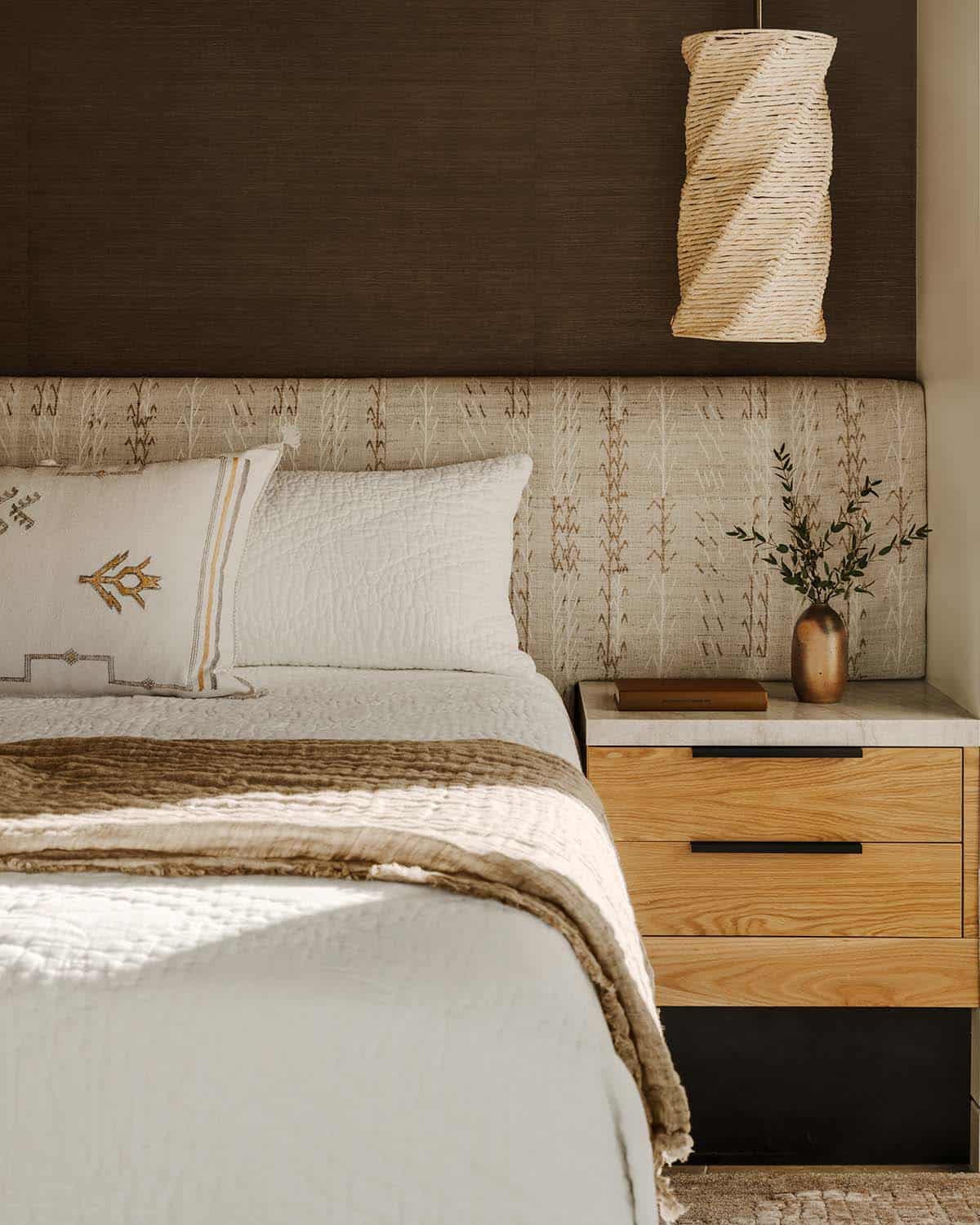 Close-up of primary bedroom headboard with tribal-pattern upholstery, linen bedding, and twisted rattan pendant light above oak nightstand