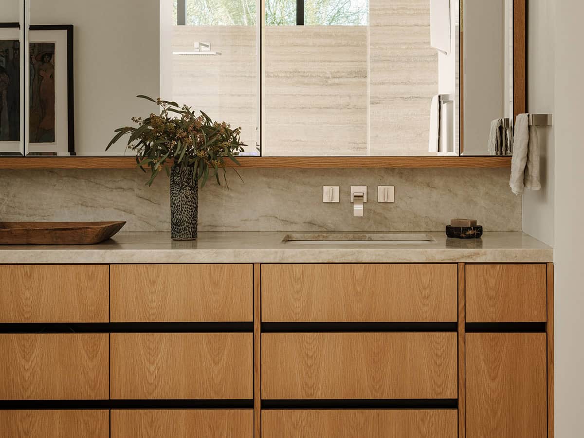 Primary bathroom vanity with oak cabinetry, veined stone countertop, wall-mount faucet, and wood-framed mirror