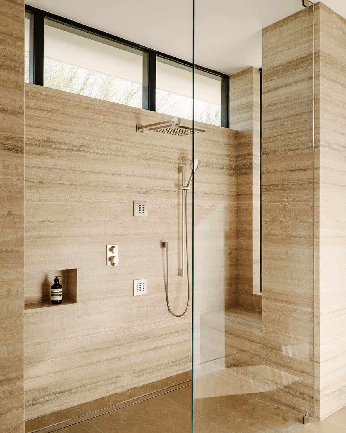 Walk-in shower clad floor-to-ceiling in travertine with rain showerhead, handheld wand, and clerestory window