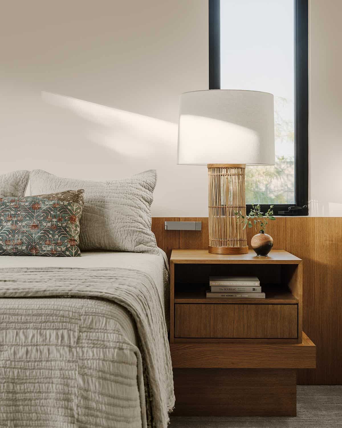 Guest bedroom detail with quilted gray bedding, botanical-print pillow, rattan table lamp, and oak floating nightstand