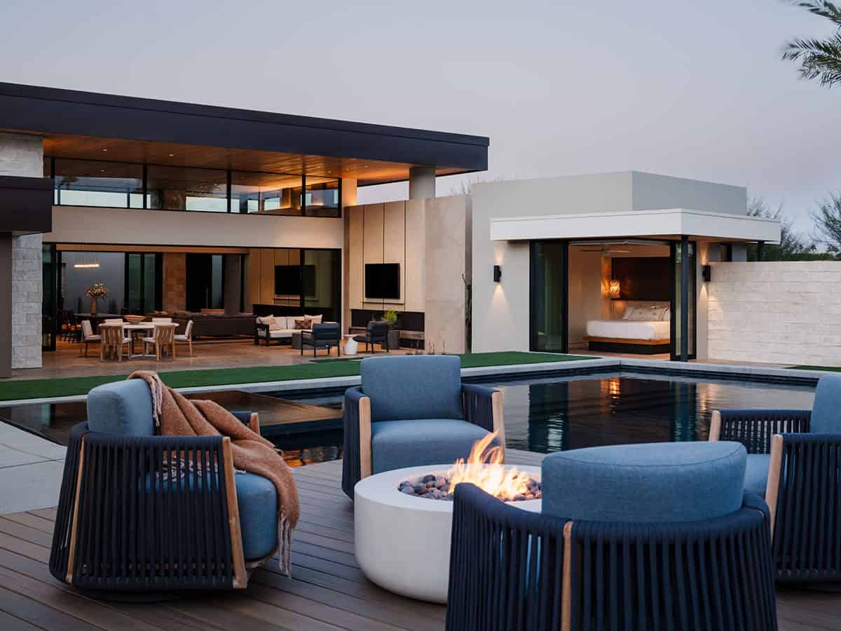 Pool deck at dusk with navy rope lounge chairs around a round fire pit, overlooking a reflecting pool