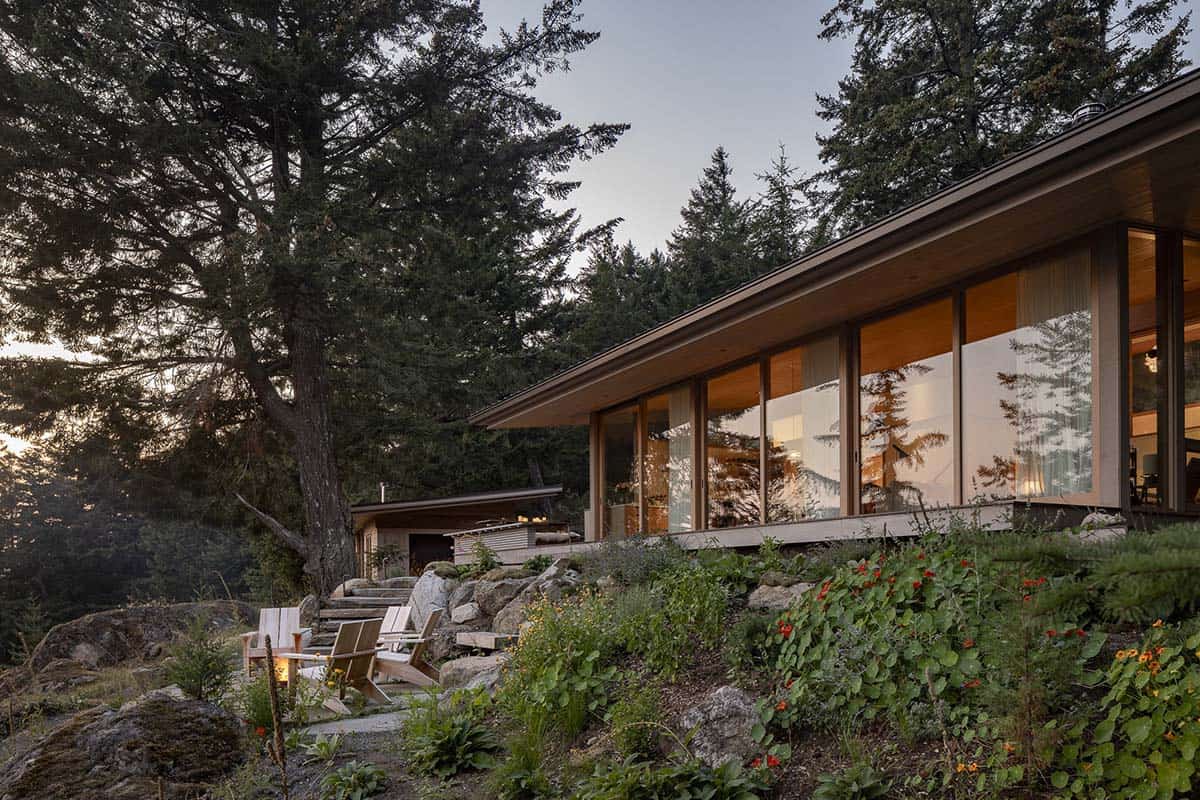 Modern hillside home exterior at dusk with floor-to-ceiling windows and rocky hillside garden, Orcas Island