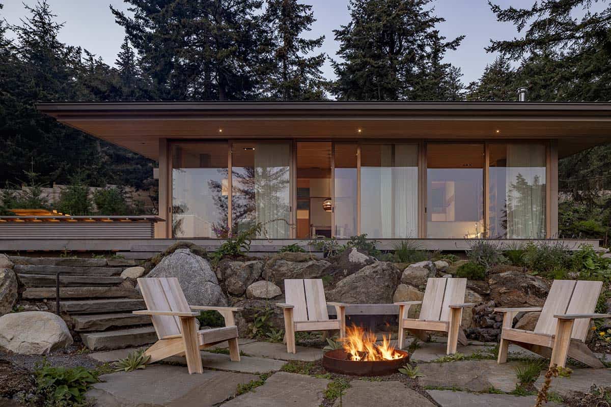 Outdoor fire pit patio with wood Adirondack chairs beside modern home with sliding glass doors, Orcas Island