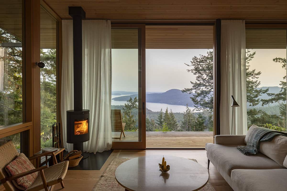 Living room with wood-burning stove and panoramic sliding glass doors opening to water views, Orcas Island
