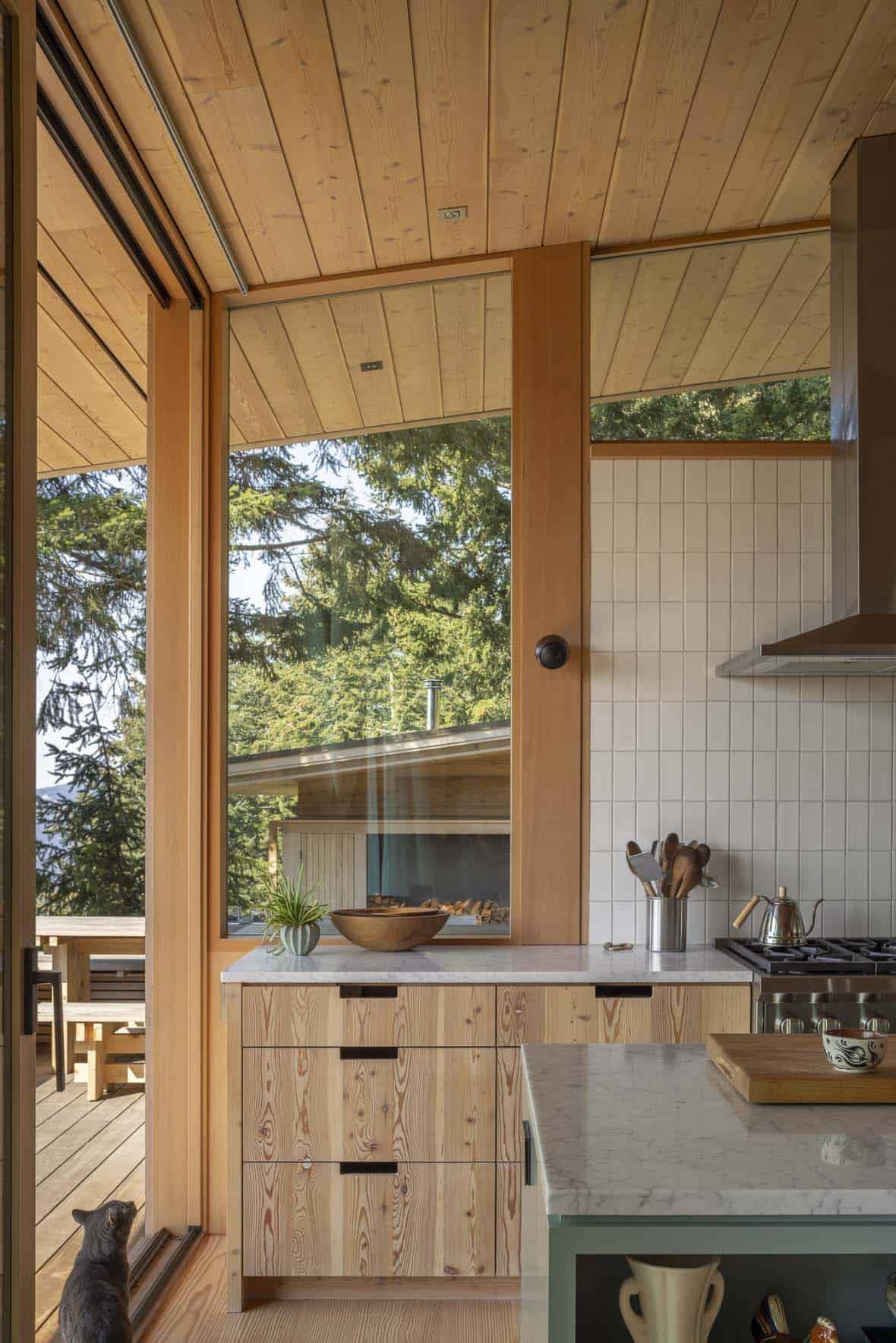 Kitchen with Douglas fir cabinetry, marble countertop, and tall window overlooking forested hillside