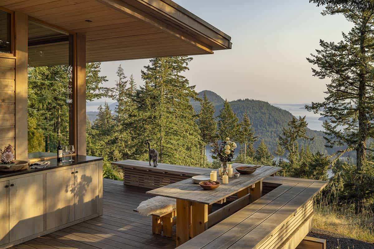 Covered outdoor deck with wood dining table and benches, outdoor kitchen, and island water views at golden hour