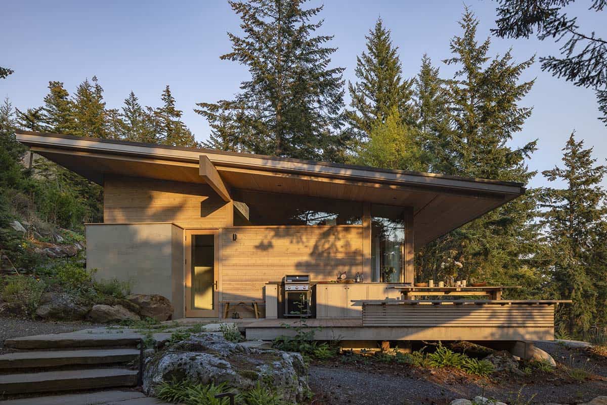 Cedar-clad modern cabin exterior with shed roof and covered outdoor kitchen deck nestled in Douglas fir forest