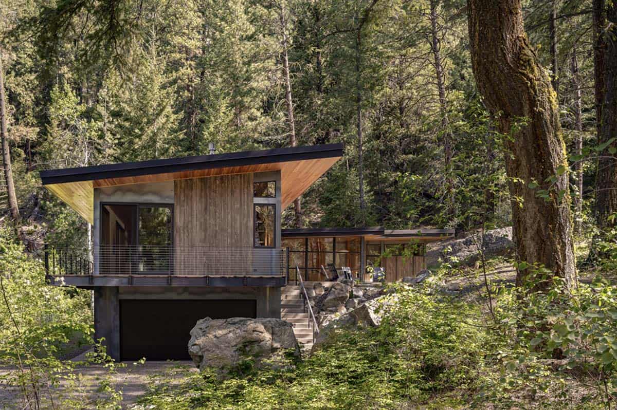 Wood-clad hillside house with shed roof and garage below, forest setting