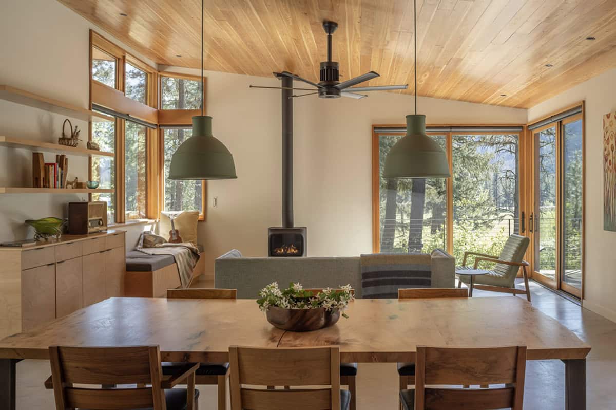 Open-plan dining and living room with wood ceiling, gas stove, and green pendant lights