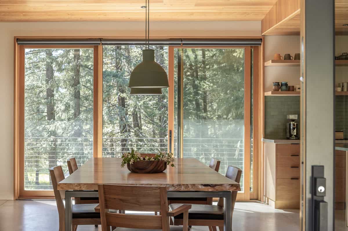 Dining area with live-edge table, green pendant light, and sliding glass doors to forest