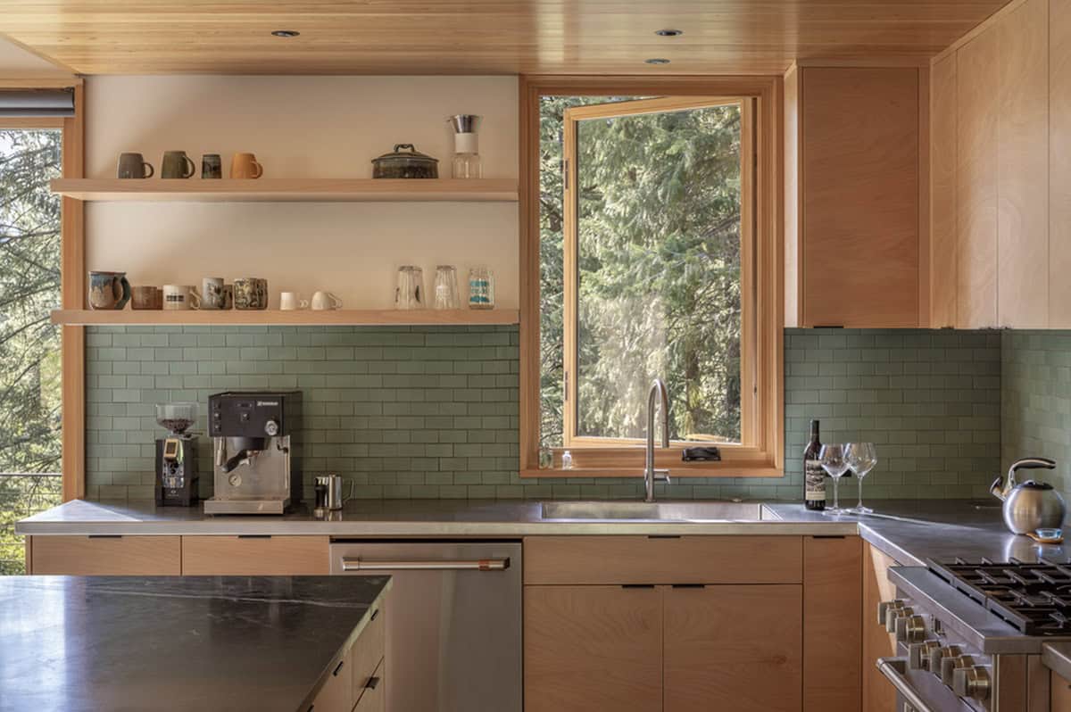 Kitchen detail with green subway tile backsplash, open shelving, and forest window
