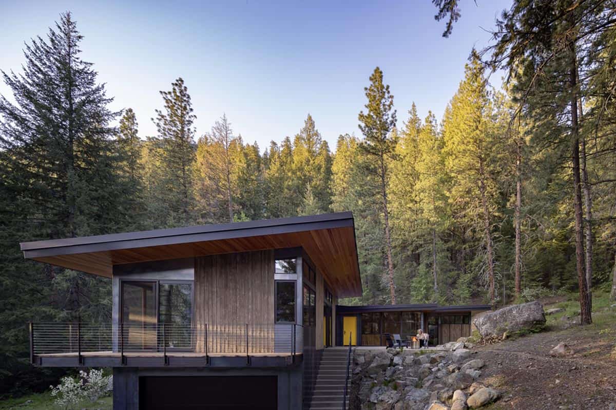 Dusk exterior view of hillside house with shed roof and glowing yellow door