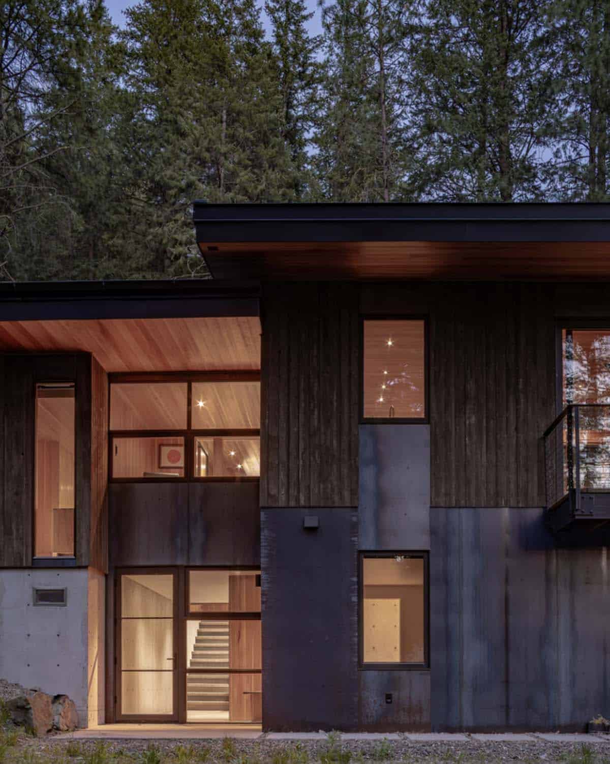 Night exterior of hillside house entry with warm interior light and steel cladding